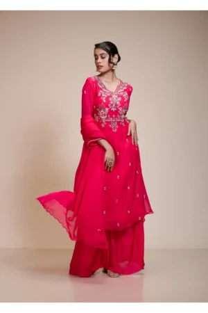 Woman wearing a vibrant rani pink A-line kurta with sharara pants and matching dupatta, featuring intricate floral hand embroidery with sequins, beads, and threadwork.